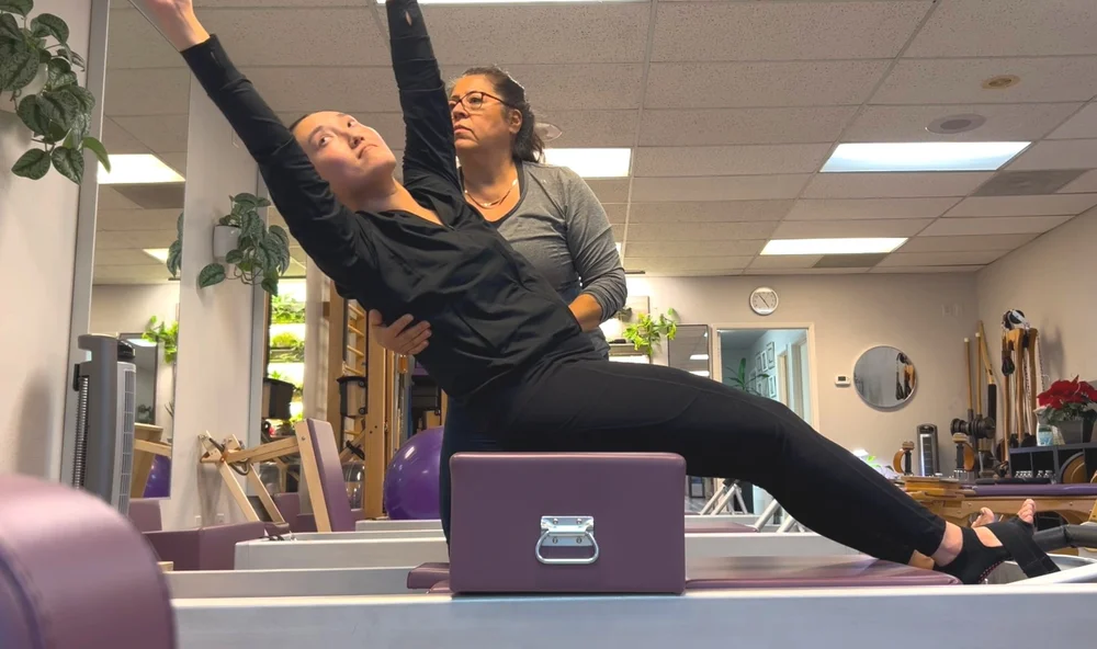 An instructor supporting a student through a stretch on the reformer